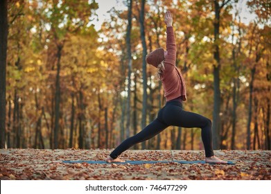Beautiful young woman practices yoga asana Virabhadrasana 1 - warrior pose on the wooden deck in the autumn park. - Shutterstock ID 746477299