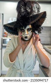 Beautiful Young Woman Prepares For The Carnival And At Home In A White Robe Tries On A White Mysterious Venetian Mask