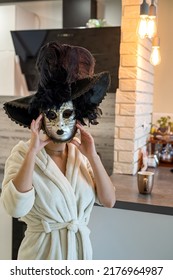 Beautiful Young Woman Prepares For The Carnival And At Home In A White Robe Tries On A White Mysterious Venetian Mask