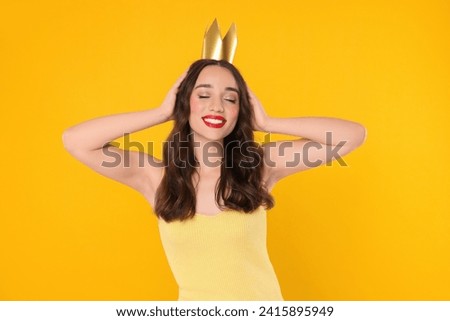 Beautiful young woman with princess crown on yellow background