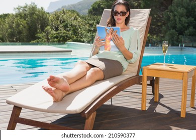 Beautiful Young Woman Reading Book On Sun Lounger By Swimming Pool