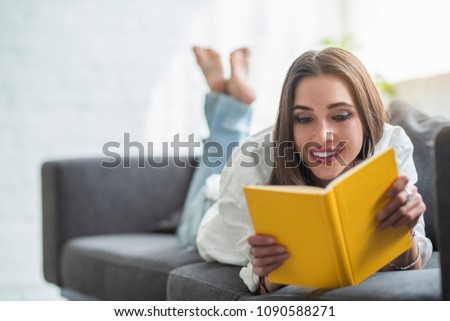 a beautiful young woman is reading a book while seating in her living room