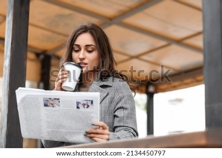 Beautiful young woman reading newspaper and drinking coffee in street cafe