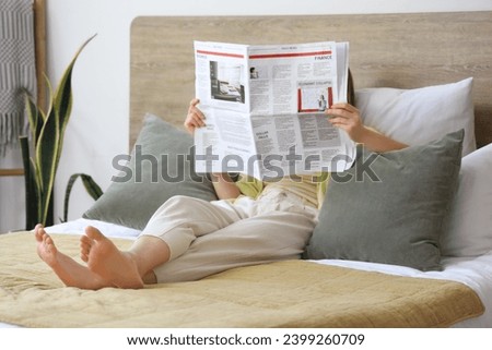 Beautiful young woman reading newspaper in bedroom at home