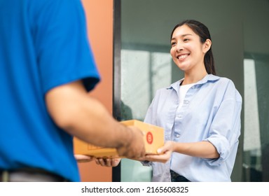 Beautiful Young Woman receiving parcel from blue uniform delivery man f the house with good service from shopping online. Courier man delivering a cardboard box postal package to destination. - Shutterstock ID 2165608325