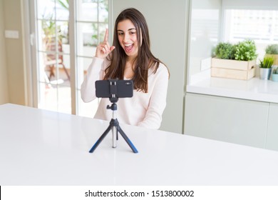 Beautiful Young Woman Recording Selfie Video With Smartphone Webcam Pointing Finger Up With Successful Idea. Exited And Happy. Number One.