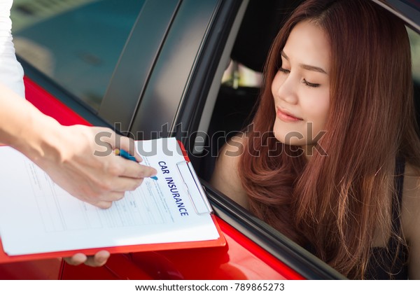 Beautiful young woman in red car is\
talking to car insurance salesman.  Car insurance\
concept.