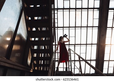 Beautiful young woman in red dress standing on ladder and looking at binoculars in greenhouse - Powered by Shutterstock