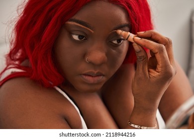 Beautiful young woman with red hair applying concealer at her face