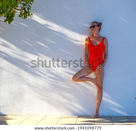 beautiful young woman in a red swimsuit against a white wall background