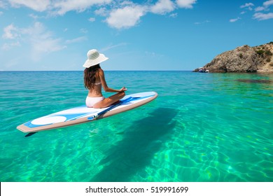 A beautiful young woman relaxes on a SUP board in the sea near the island. Standup paddleboarding on Hawaii. 