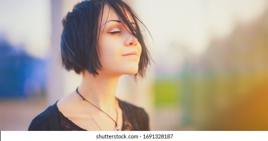 Beautiful young woman relaxing and enjoying sun at sunset. Beauty sunshine girl side profile portrait. Pretty happy woman enjoying summer outdoors. Positive emotion life success mind peace concept.