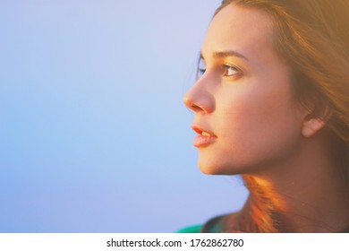 Beautiful young woman relaxing and enjoying sun at sunset. Beauty sunshine girl side profile portrait. Pretty happy lady enjoying summer outdoors. Positive emotion life success mind peace concept.