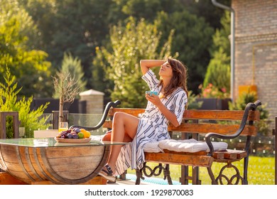 Beautiful young woman relaxing on the terrace in the backyard of her home, drinking morning coffee and enjoying sunny summer day outdoors - Powered by Shutterstock