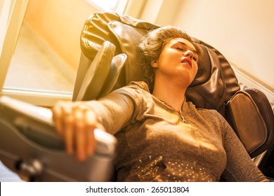 Beautiful Young Woman Relaxing On The Massage Chair In Living Room.