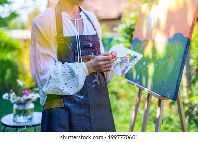 Beautiful young woman relaxing while painting an art canvas outdoors in her garden. Mindfulness, art therapy, creativity concept.