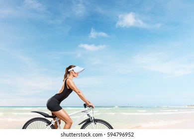 Beautiful Young Woman Riding On Bicycle With White Sand Beach And Sea In Background