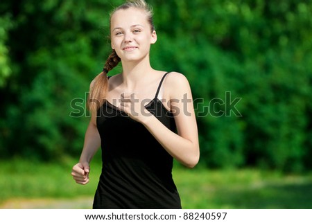 Beautiful young woman running in green park on sunny summer day