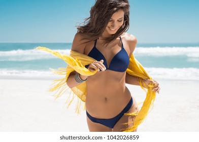 Beautiful young woman running on the beach with a yellow tissue. Happy smiling girl with scarf enjoying at beach. Freedom and carefree concept.