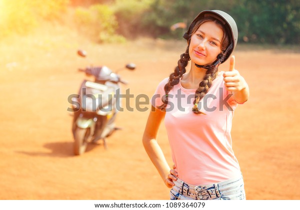 beautiful and young woman in a safety helmet
stands in front of a motorcycle (bike) and shows a thumb finger up.
concept of safe driving a
scooter