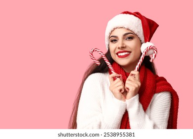 Beautiful young woman in Santa hat with Christmas candy canes on pink background - Powered by Shutterstock