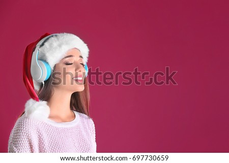 Beautiful young woman in Santa hat listening to Christmas music on color background