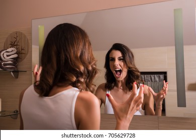 A beautiful young woman screaming in the mirror in the bathroom