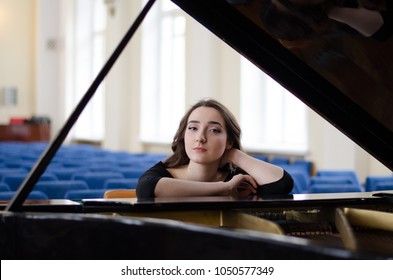 Beautiful young woman seating next to grand piano alone in concert hall during daytime