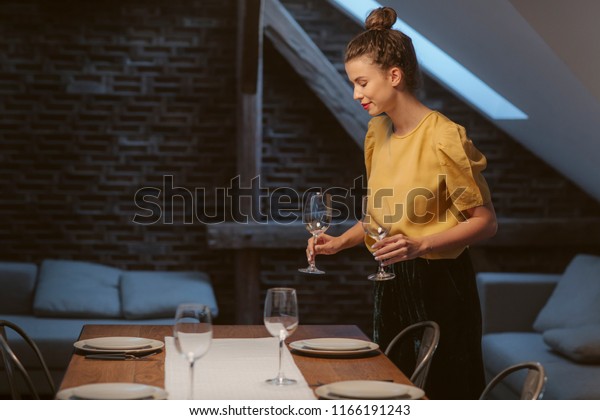 Beautiful young woman setting up table for dinner\
party at home.