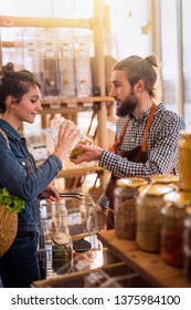 Beautiful Young Woman Shopping In A Bulk Food Store. The Seller Advises Her To Buy Organic Spices In Jars.