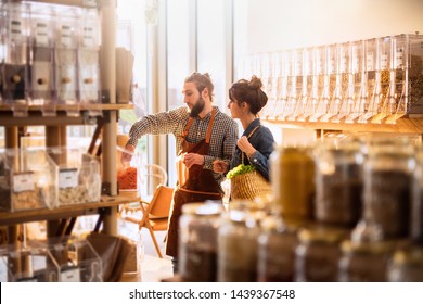 Beautiful Young Woman Shopping In A Bulk Food Store. The Seller Advises Her On Her Purchases Of Organic Food