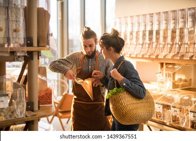 Beautiful Young Woman Shopping In A Bulk Food Store. The Seller Advises Her On Her Purchases Of Organic Food