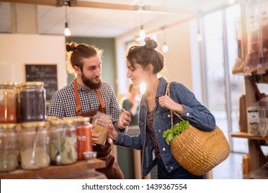 Beautiful young woman shopping in a bulk food store. The seller advises her to buy organic spices in jars.