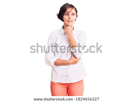 Beautiful young woman with short hair wearing elegant white shirt with hand on chin thinking about question, pensive expression. smiling with thoughtful face. doubt concept. 