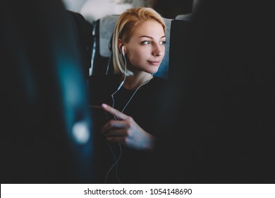Beautiful young woman with short haircut listening favorite audio songs in modern earphones resting during flight and enjoying comfort first class sitting in seat on airplane board