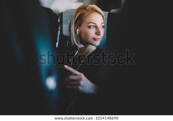 Beautiful young\
woman with short haircut listening favorite audio songs in modern\
earphones resting during flight and enjoying comfort first class\
sitting in seat on airplane\
board