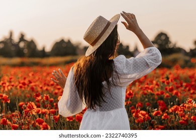 Beautiful young woman in short white dress and straw hat in field with poppies in evening at sunset and holds poppy in hand, Summer countryside nature flowers, Female relaxing, Rural simple life - Powered by Shutterstock