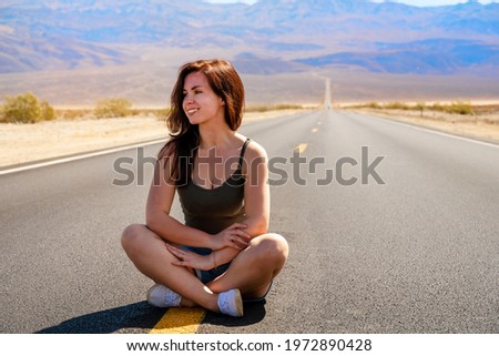 Beautiful young woman in shorts sits on a picturesque empty road in Death Valley, USA