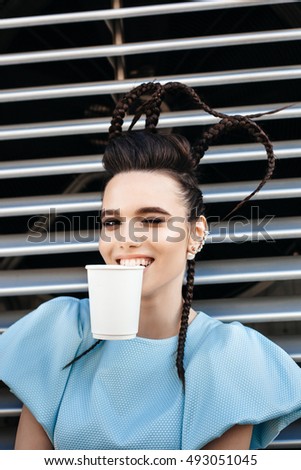 Beautiful young woman showing hot drink in disposable paper cup. Outdoors lifestyle portrait of girl having fun