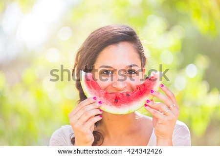 Beautiful young woman showing a slice of watermelon as a smile. She is caucasian, she wear a white dress and she has a braid on the shoulder. Summer and lifestyle concepts.