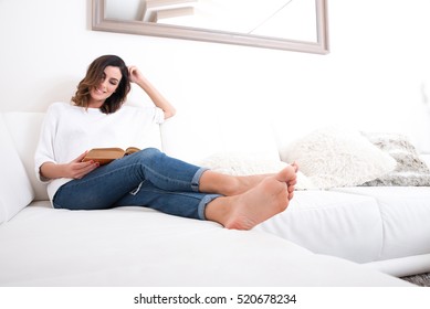 A Beautiful Young Woman Siting On A Couch And Reading A Book.