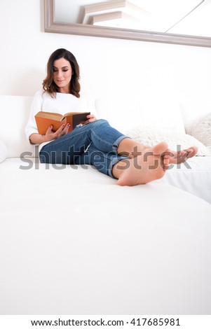 A beautiful young woman siting on a couch and reading a book.