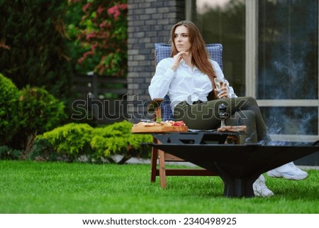 Beautiful young woman sits on folding chair on backyard and looking to the side