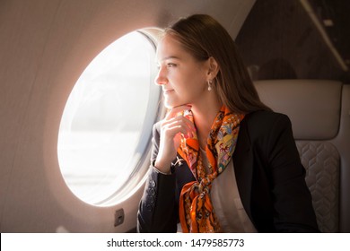 Beautiful Young Woman Sits In A Plane Near The Window And Look Outside At Sunny Day