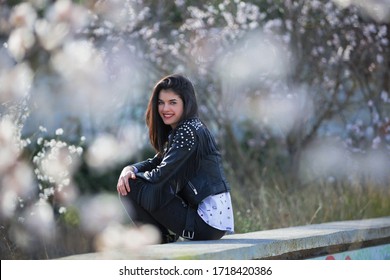 Beautiful Young Woman Sitting In An Abandoned Pool Among Cherry Blossoms Smiling