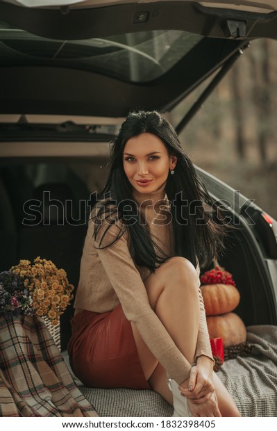 Beautiful young woman sitting in the back of car\
and enjoying autumn atmosphere in forest. Travel fashion and\
beauty, lifestyle\
concept
