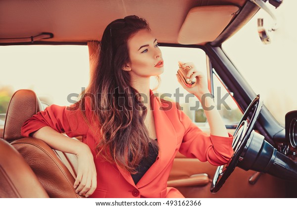 Beautiful young woman sitting behind the wheel in\
retro automobile using a\
perfume