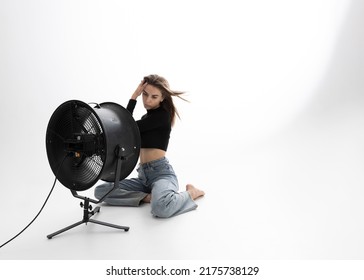 A Beautiful Young Woman Is Sitting In A Bright Room On The Floor Cooling Down Under A Fan