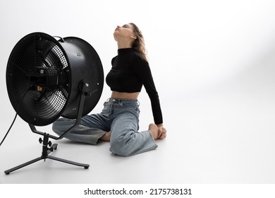 A Beautiful Young Woman Is Sitting In A Bright Room On The Floor Cooling Down Under A Fan