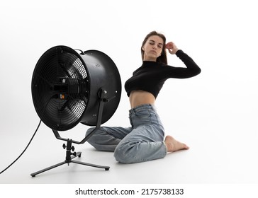 A Beautiful Young Woman Is Sitting In A Bright Room On The Floor Cooling Down Under A Fan